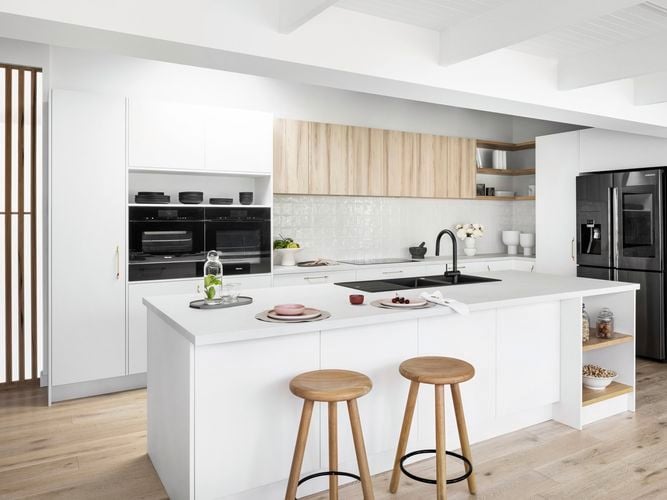 Modern light themed kitchen with appliances, island benchtop and timber stools.
