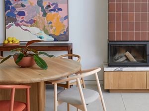 Modern dining area with a round wooden table and chairs, a white pendant light, a colourful abstract painting, and a built‑in fireplace clad in terracotta tiles with a black flue and timber base cabinet.