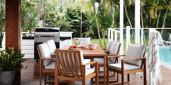A red stained outdoor dining set on a matching red stained deck, with a pool nearby