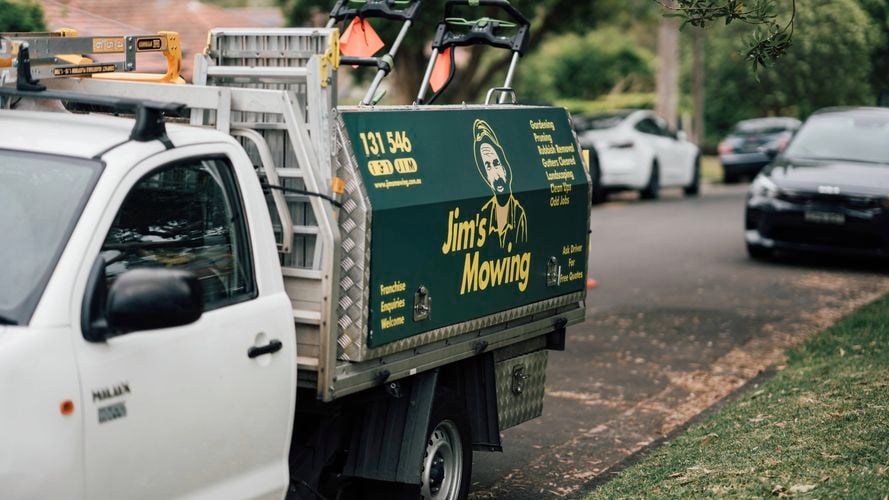 Person using a Makita miter saw on a yellow stand to cut wood, wearing a 'BANKS CARPENTRY' shirt.