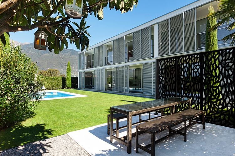 Backyard to large home with grass, pool, outdoor dining table and decorative screens