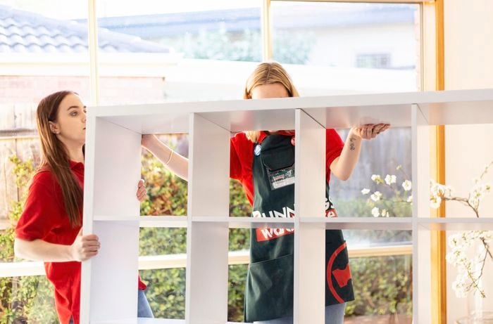 Two people carrying a cube storage room divider