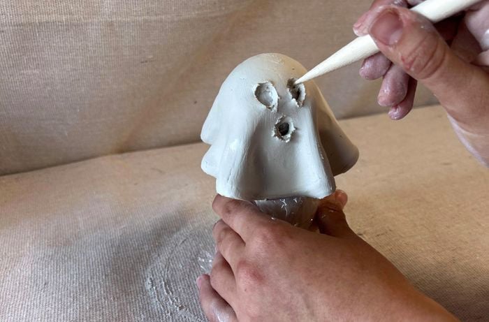 A wooden carving tool is used to cut out eyes and mouth from a clay ghost form.