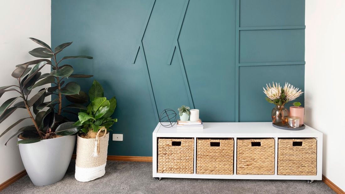 Room with green wall, plants and cube storage unit with wicker basket inserts.