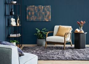 Close up shot of armchair in living room setting next to side table, plants and painting on wall.