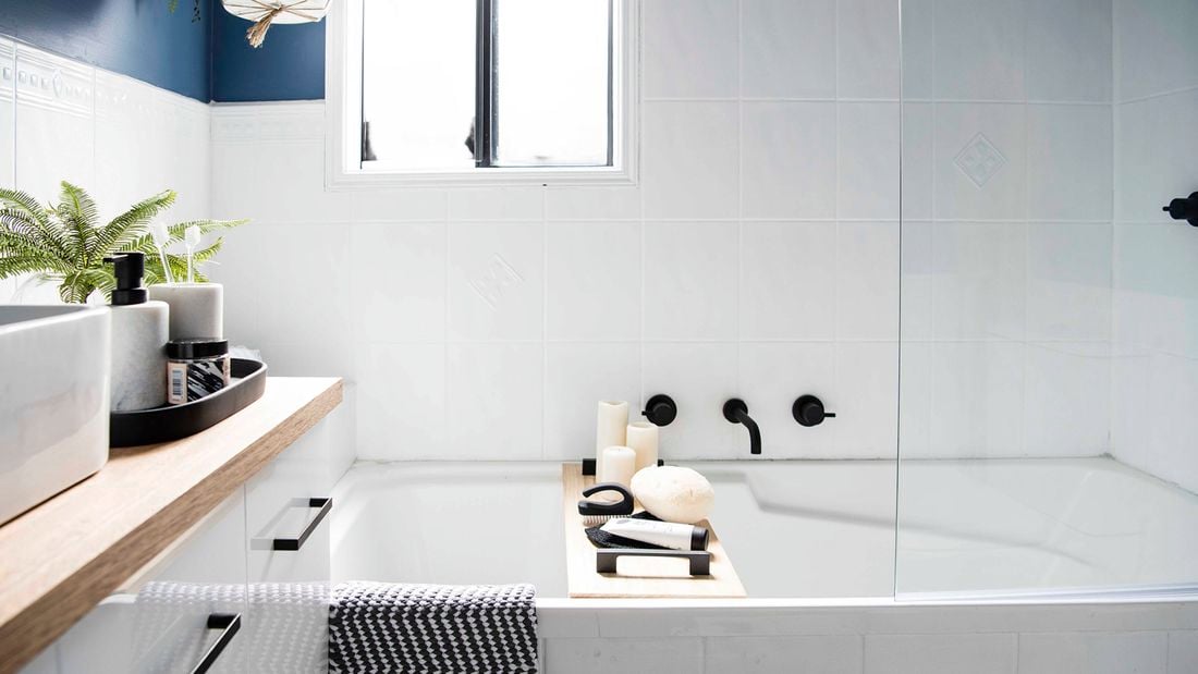 A white tiled bathroom, with black tapware over a white bath and a deep blue feature wall showcasing a bathroom design idea.