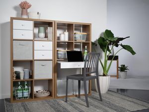 A shelving unit next to a wall with shelves and drawers in it, a plant next to it and a chair in front of it