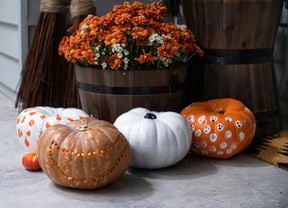 Close up of three decorated pumpkins in front of a potted plant in a barrel.