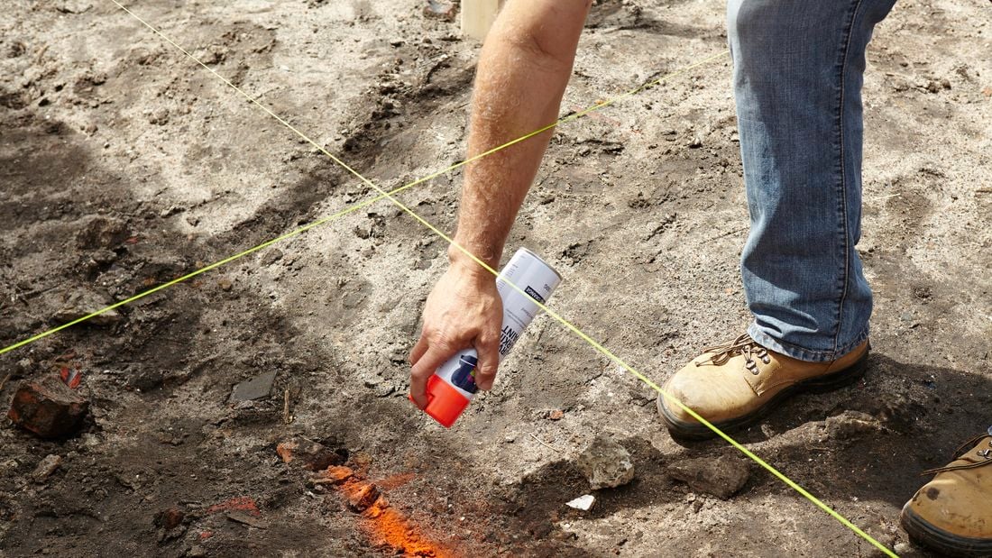 An orange paint spray can being used to mark bare earth for a foundation dig site