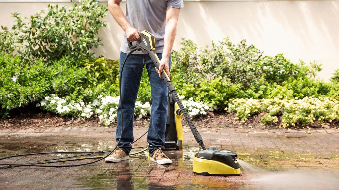 A man cleaning a paved outdoor floor with a Pressure washer and surface cleaner accessory.