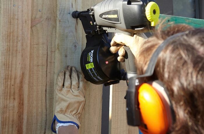 Person installing fence paling with nail gun.