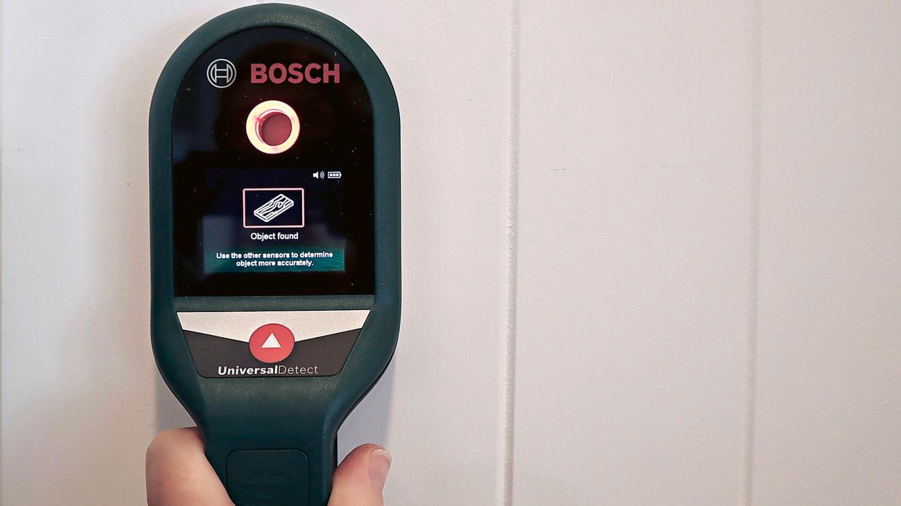 A person holding a Bosch stud finder up to a wall.