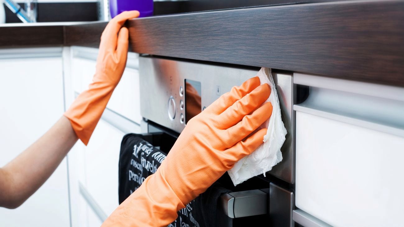 Hands wearing orange rubber gloves cleaning the outside of an oven