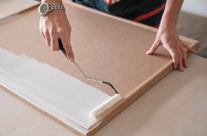 A person painting the cabinetry using a paint brush.