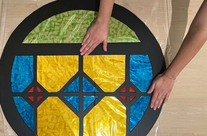A pair of hands presses the black flute board window cutout onto the self-adhesive film