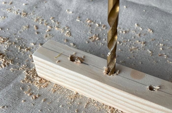 Drill bit creating holes in a pine piece.