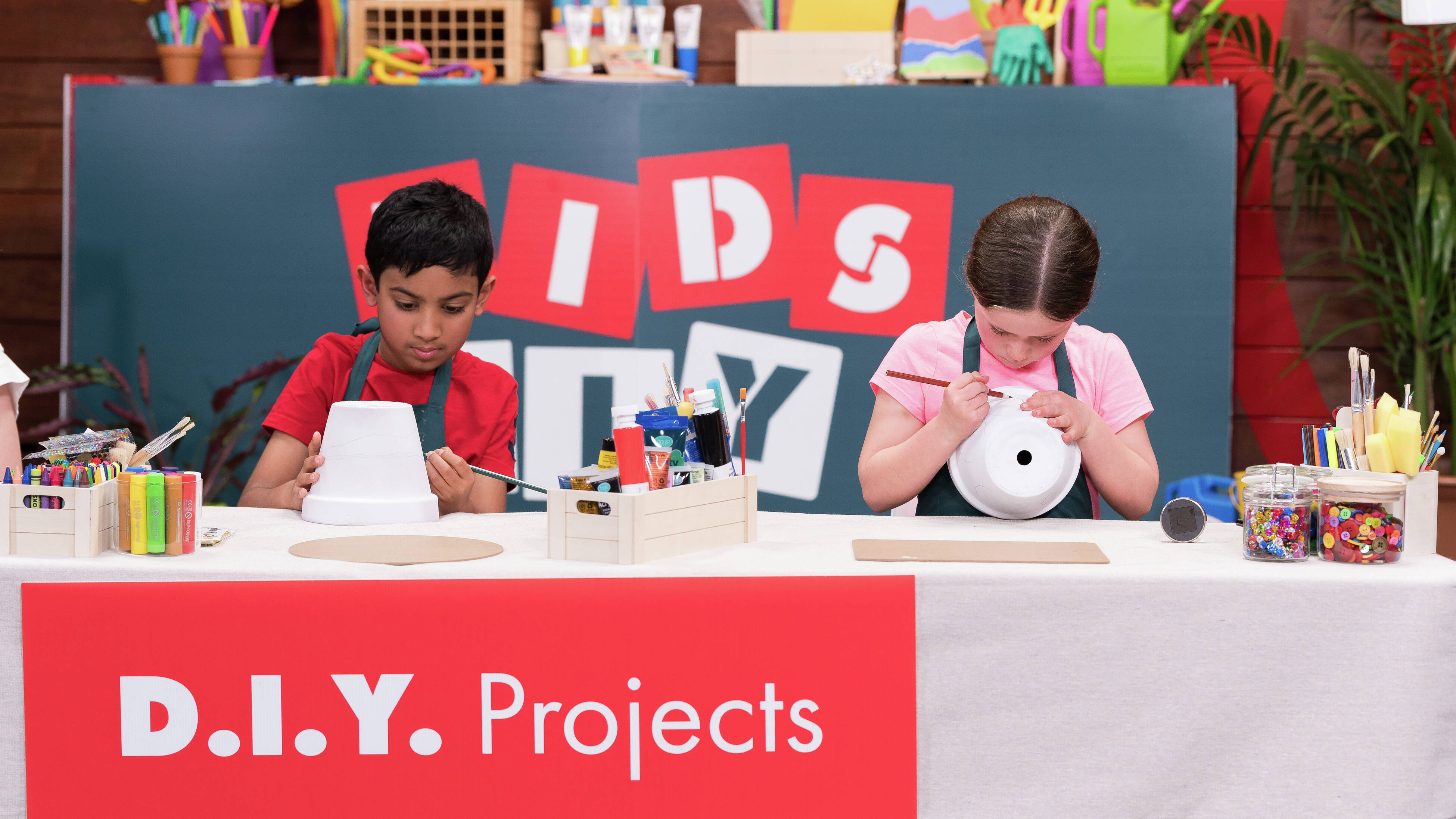 Two kids are sketching on a pot with pencils at a Bunnings kids' DIY workshop.