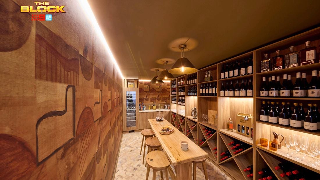 A bar area with lot of bottles of wine in it with a table and stools around it.