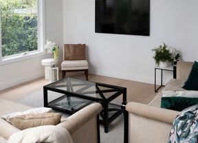 An image of a room featuring a couch, a glass table in front of it, and a TV mounted on the wall.