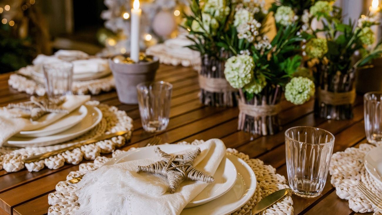 Close-up of a festive outdoor dining table with plates, candles, and floral centerpieces.