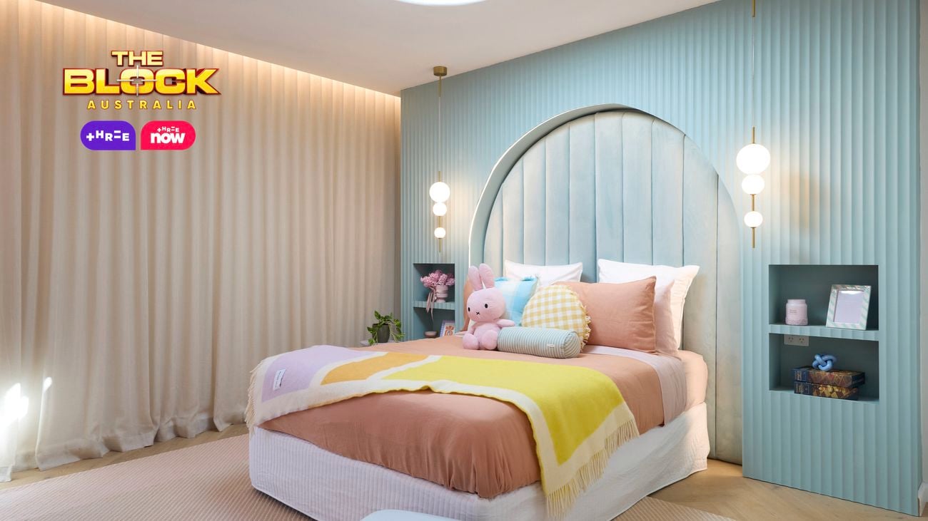 Pastel bedroom featuring a pale blue feature wall with recessed bedside tables and a double bed with pastel linen in orange, purple and yellow. 