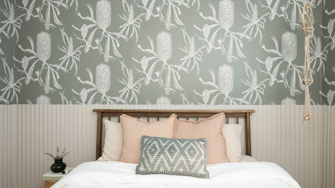 An image of a tidy room with a bed, a bedside table and modern wallpaper in the background