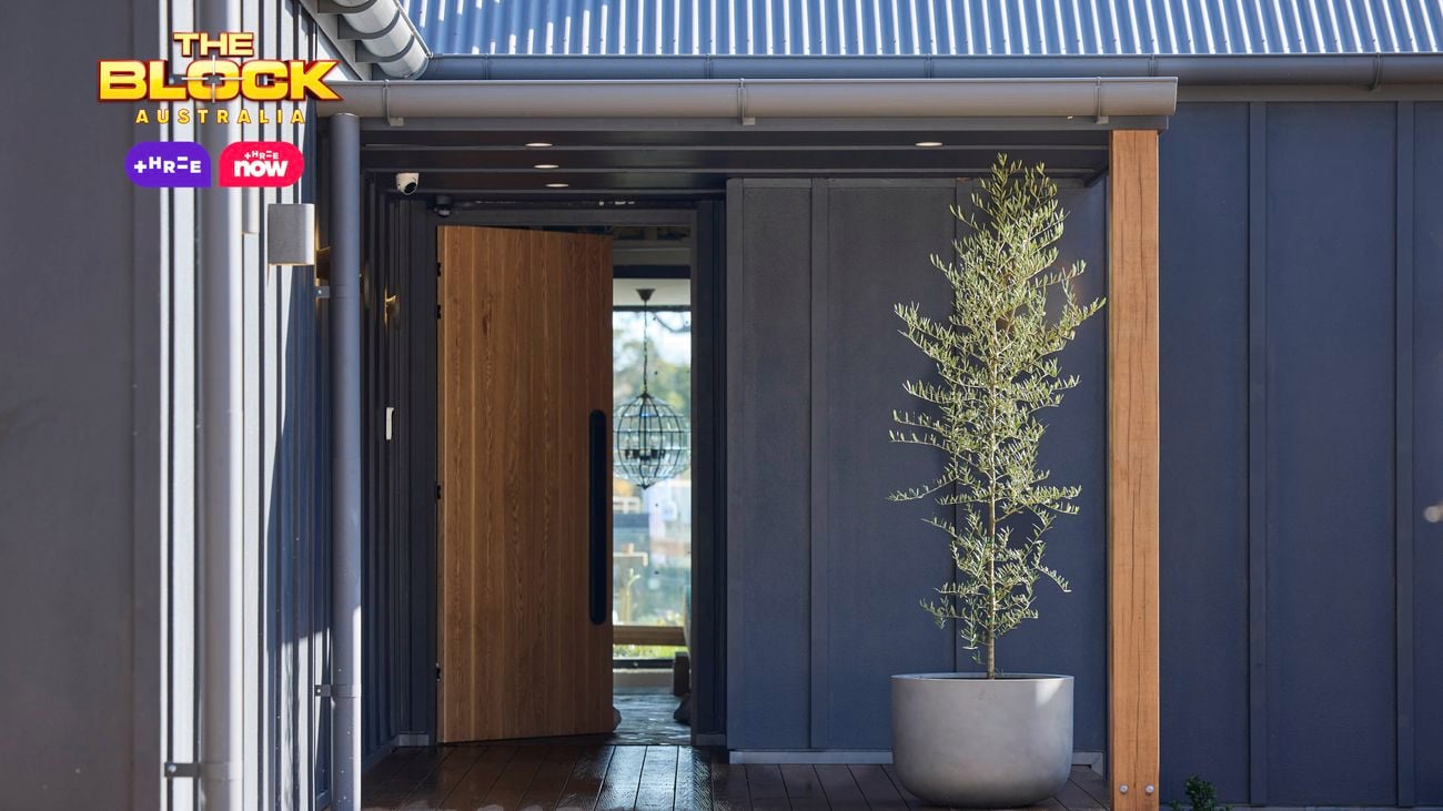 A front entrance of a house with the timber door open and a pot with a tree in it on timber decking.