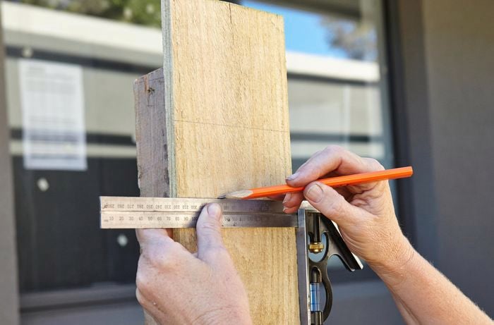 Person measuring weathered plinth with metal ruler and measuring tape.