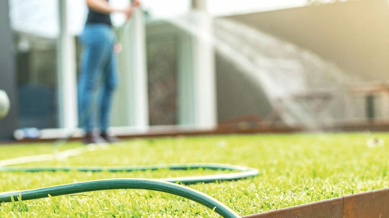 Garden hose on grass and person using hose in the background.