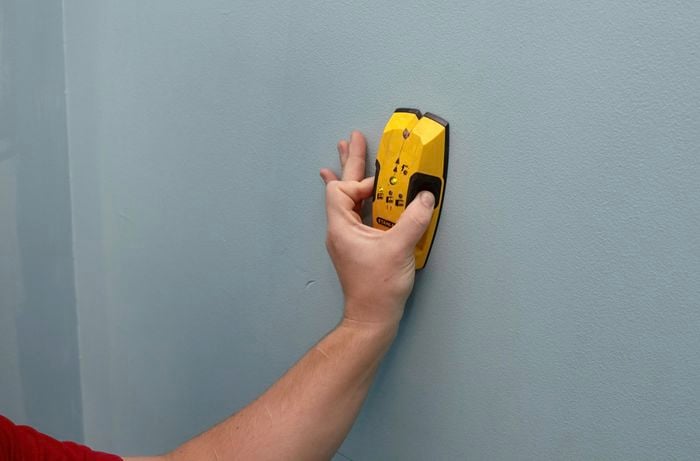 A person holding a stud finder to a wall
