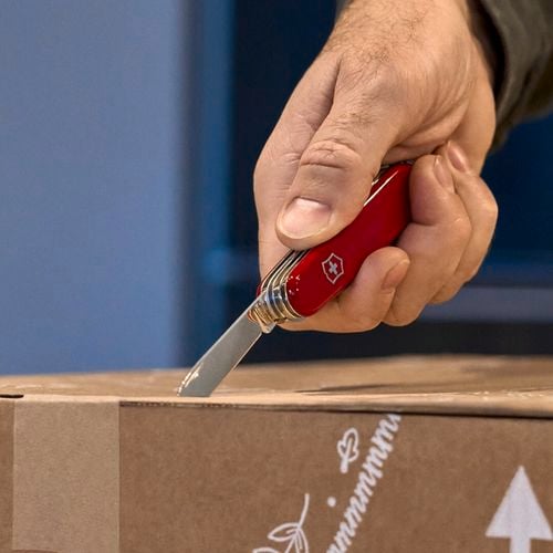 A person cutting a cardboard box with an army knife.