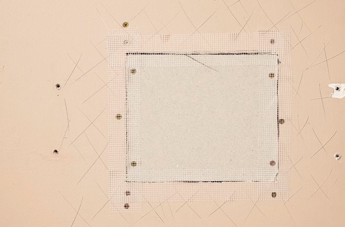 A patch is secured to a wall with joint tape, preparing it for repair
