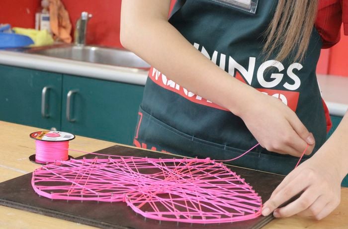 Person threading pink string around nails in plywood sheet