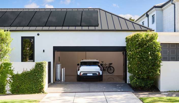 Modern home with rooftop solar panels, an electric vehicle parked in an open garage, and landscaped greenery along the driveway.