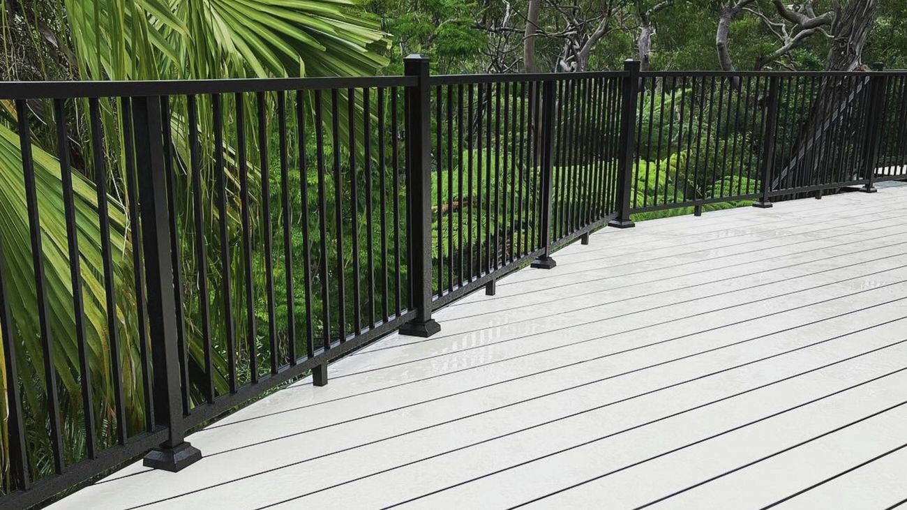 A white composite deck with black railings overlooking a lush green forest