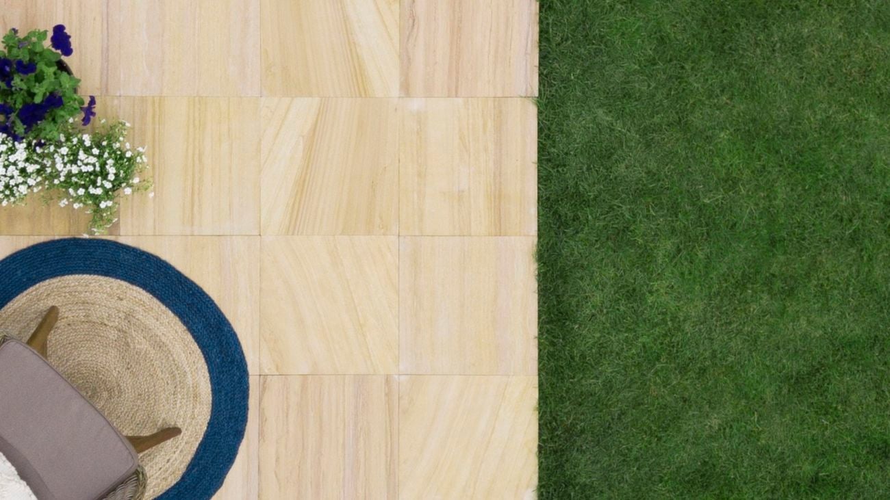 Outdoor sandstone pavers next to a lawn, with plants, an outdoor jute rug and chair