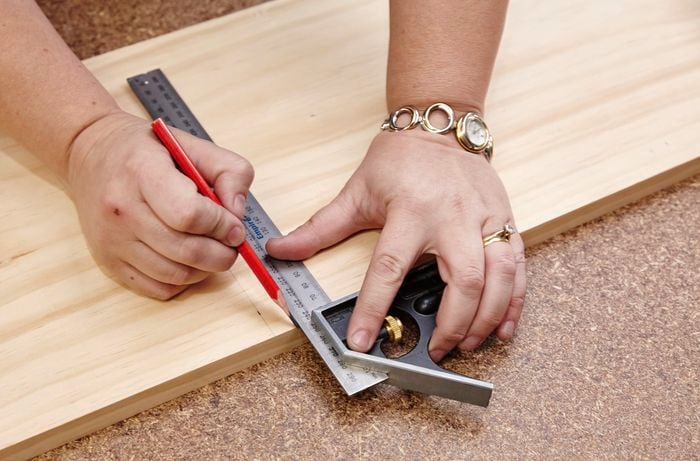 A square rule and pencil being used to mark a piece of timber for cutting