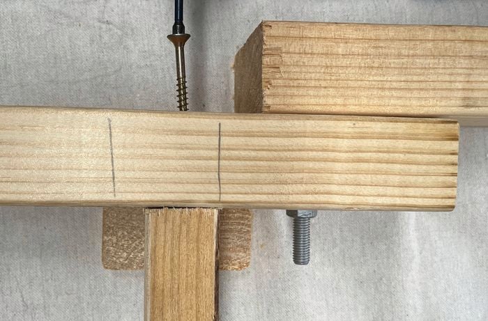 Two pieces of timber being joined with a screw, with pencil markings on the top piece.
