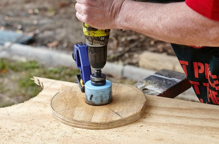 A person making a hole in a circle of plywood using a hole saw