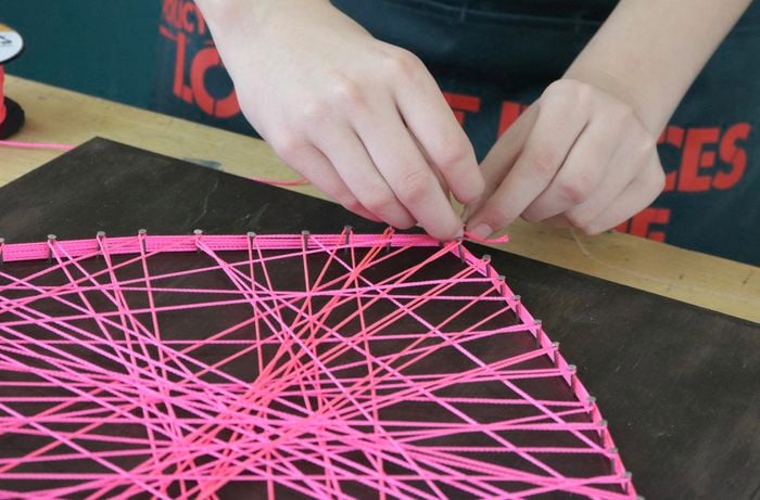 Person threading pink string around a heart shape outline