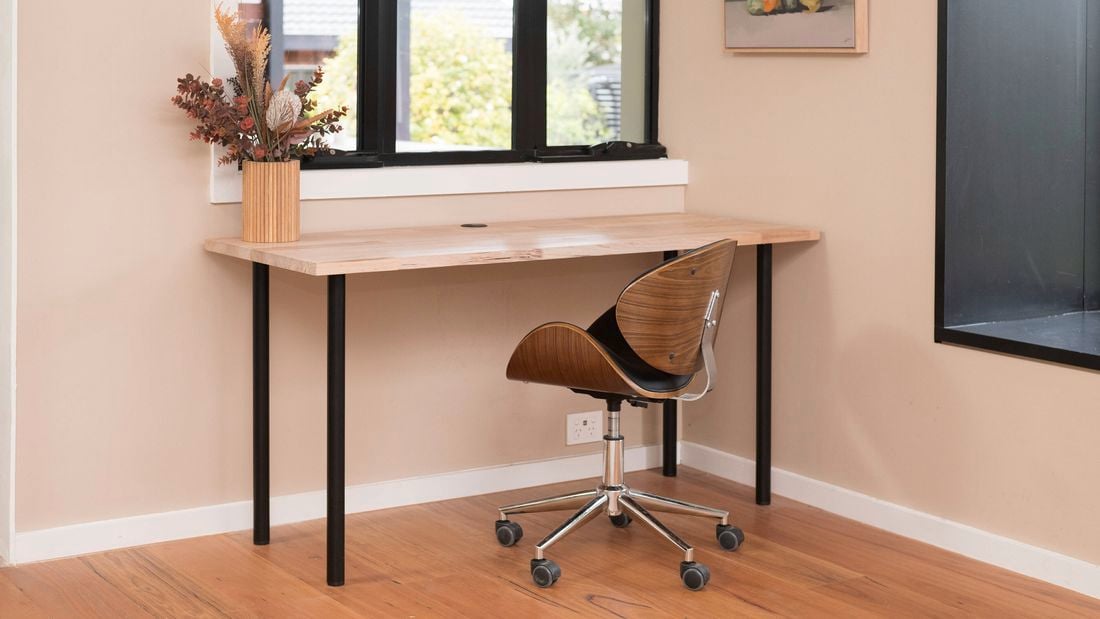 A room with a desk, chair, window, and a flower vase on the desk 