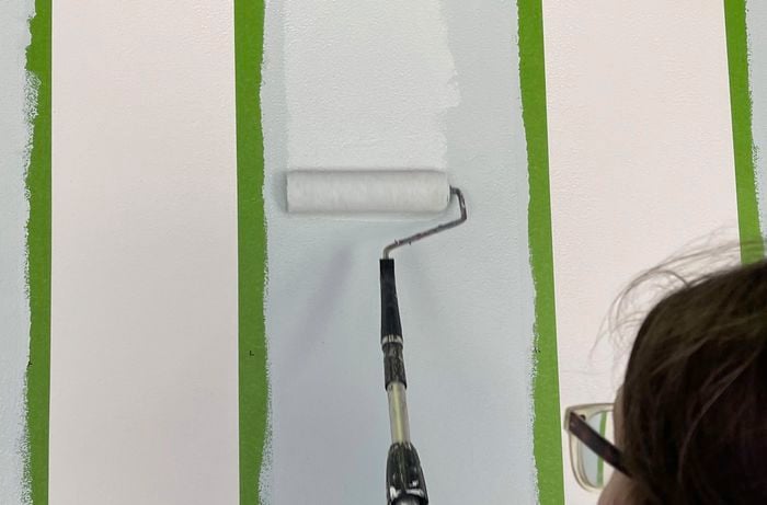 Person using paint roller to apply vertical stripes.