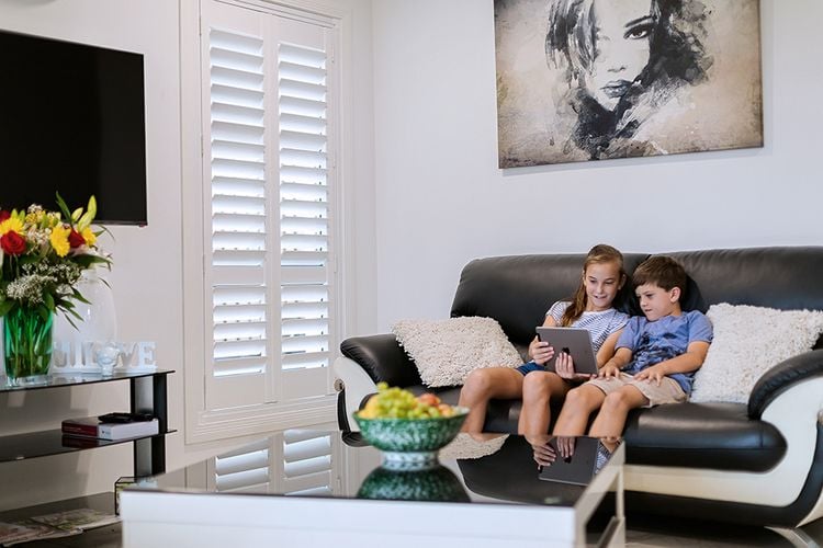 Two children using a tablet in a loungeroom with blinds