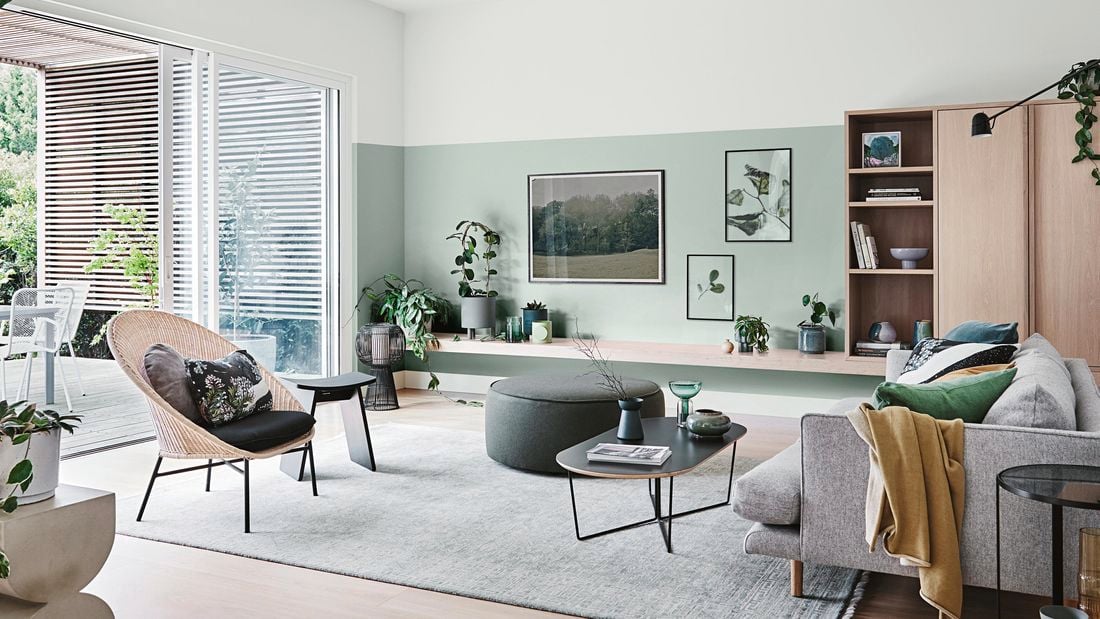 Living with couch, rug, green walls, lots of plants and paintings.