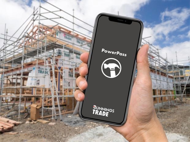 A hand holding a phone with the PowerPass app open on a construction site