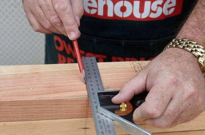 A person marking a line on a piece of timber using a set square and pencil