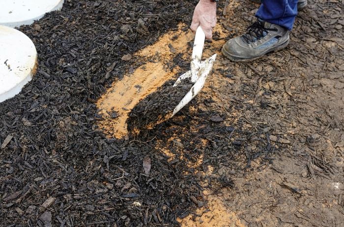 Person shovelling bark mulch around concrete pavers