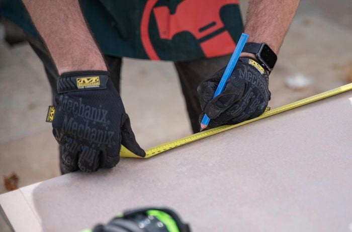 A person using a tape measure to measure the dimensions of cement sheet.