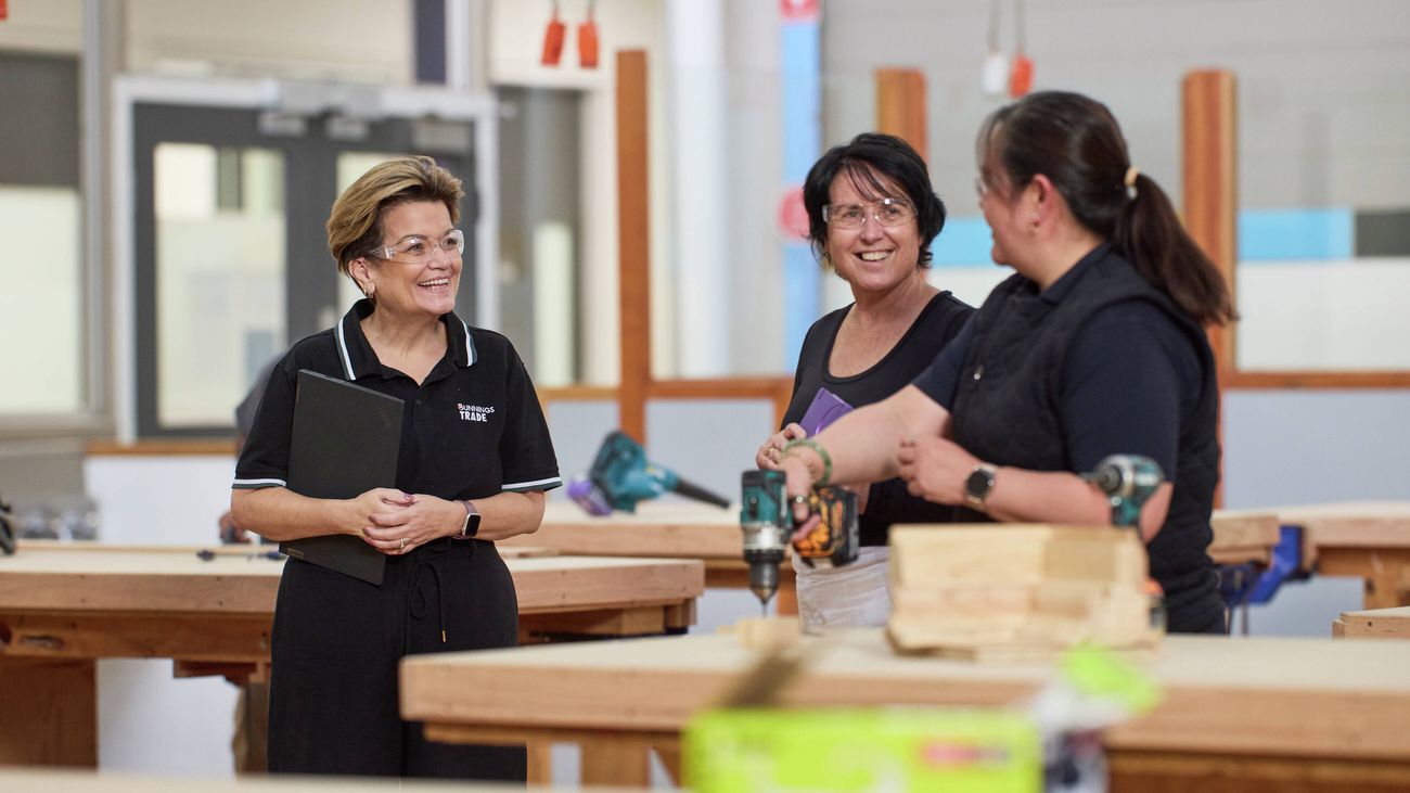 Bunnings Trade team member speaking with students in a woodworking workshop surrounded by timber workbenches and power tools.