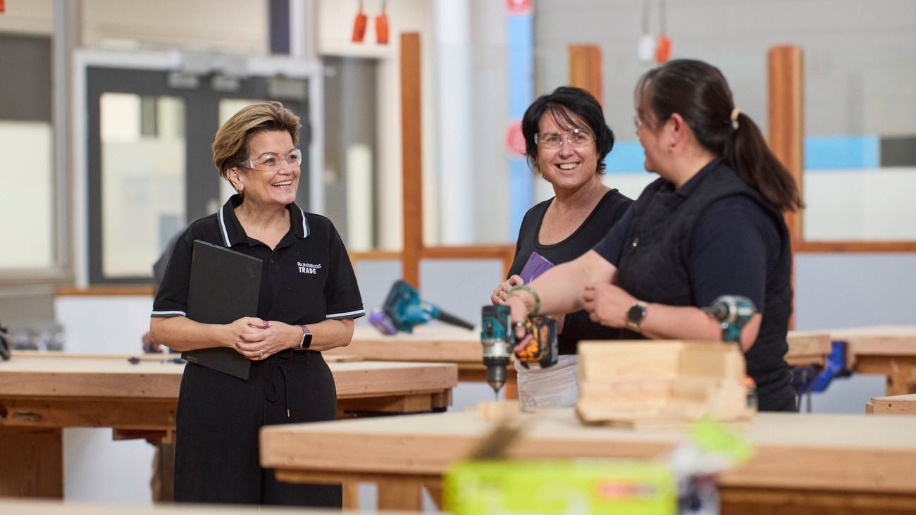 Bunnings Trade team member speaking with students in a woodworking workshop surrounded by timber workbenches and power tools.